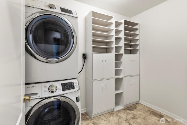 clothes washing area featuring stacked washer and dryer, baseboards, and cabinet space