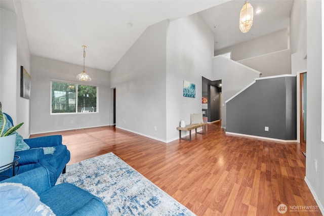 living area featuring a notable chandelier, high vaulted ceiling, wood finished floors, and baseboards