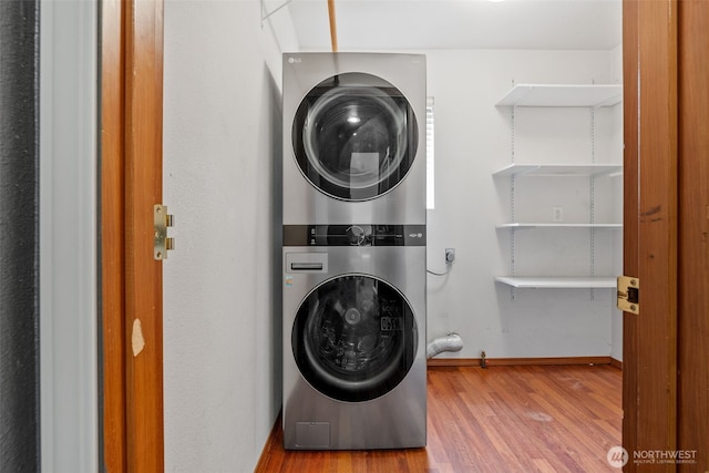 washroom featuring laundry area, stacked washing maching and dryer, baseboards, and wood finished floors