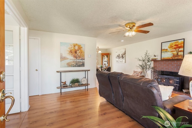 living room featuring ceiling fan, light hardwood / wood-style flooring, a textured ceiling, and a fireplace