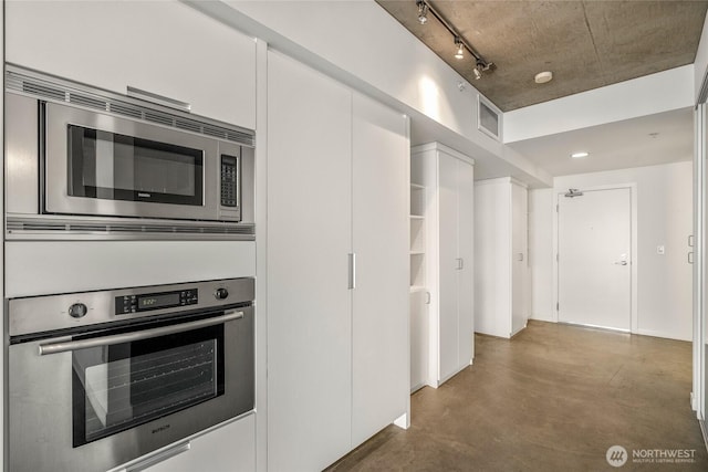 kitchen featuring visible vents, rail lighting, stainless steel appliances, concrete floors, and white cabinetry