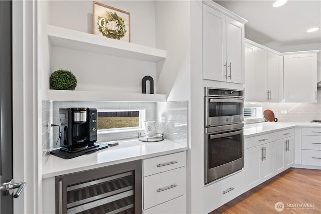 kitchen featuring light hardwood / wood-style flooring, white cabinetry, double oven, backsplash, and beverage cooler