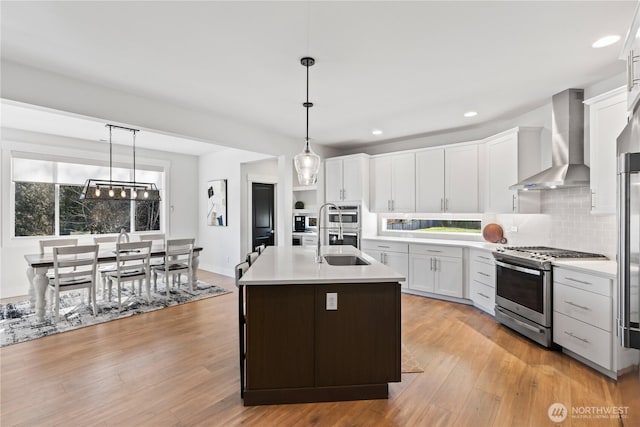 kitchen with appliances with stainless steel finishes, decorative light fixtures, an island with sink, white cabinets, and wall chimney range hood