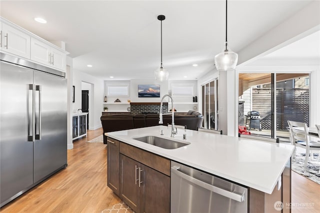 kitchen featuring sink, appliances with stainless steel finishes, white cabinetry, a center island with sink, and decorative light fixtures