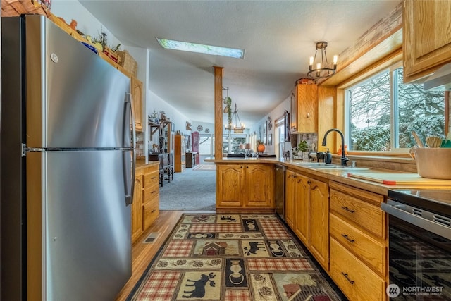 kitchen featuring pendant lighting, stainless steel refrigerator, sink, a notable chandelier, and kitchen peninsula