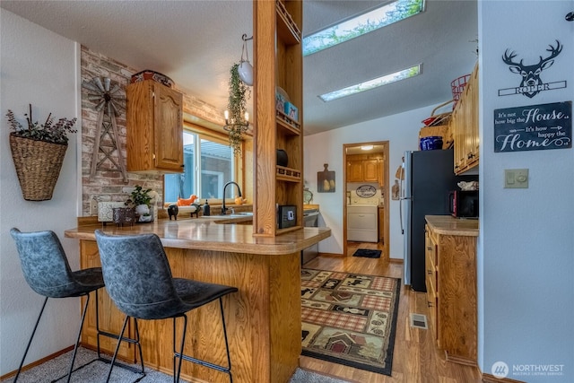 kitchen featuring kitchen peninsula, vaulted ceiling, a breakfast bar area, and light wood-type flooring