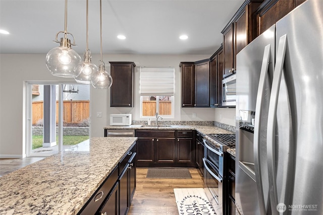 kitchen featuring stainless steel appliances, light hardwood / wood-style floors, sink, light stone counters, and pendant lighting