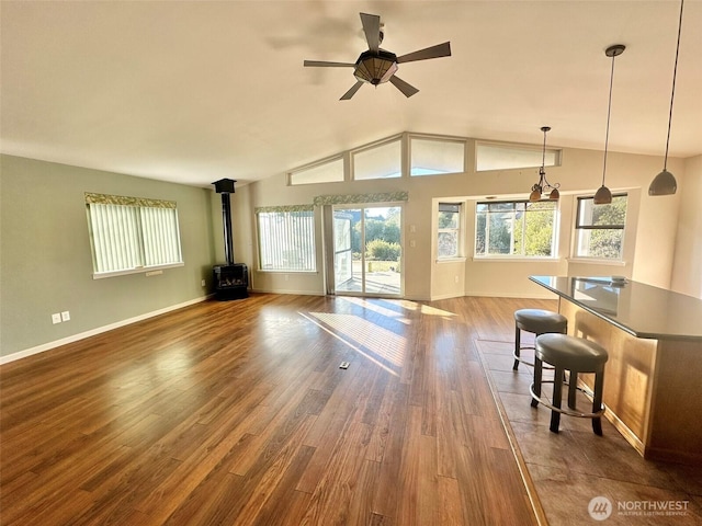 unfurnished living room featuring baseboards, ceiling fan, wood finished floors, a wood stove, and vaulted ceiling