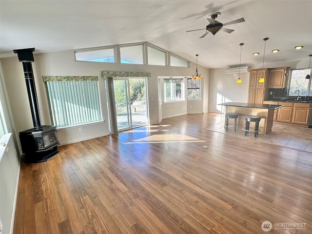 unfurnished living room with ceiling fan, a sink, light wood-style floors, vaulted ceiling, and a wood stove