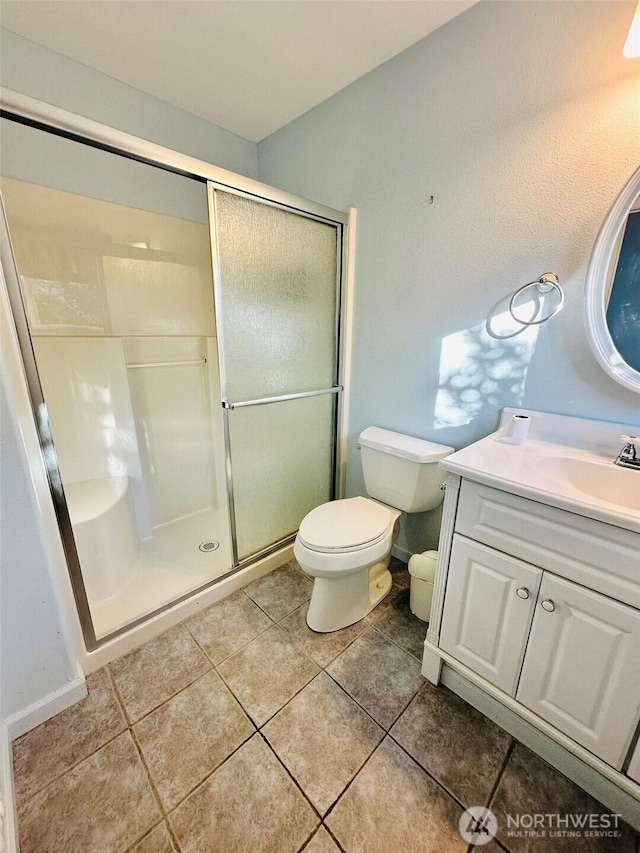 bathroom with tile patterned flooring, toilet, vanity, baseboards, and a stall shower