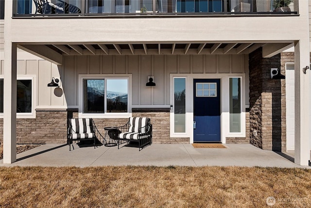 doorway to property featuring board and batten siding, stone siding, and a patio