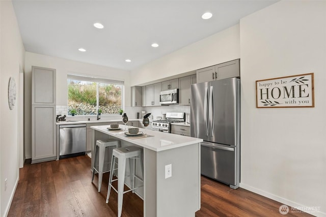 kitchen featuring a kitchen island, appliances with stainless steel finishes, a breakfast bar area, gray cabinetry, and backsplash