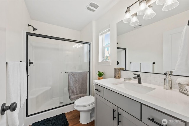 bathroom with a shower with shower door, tasteful backsplash, hardwood / wood-style flooring, vanity, and toilet