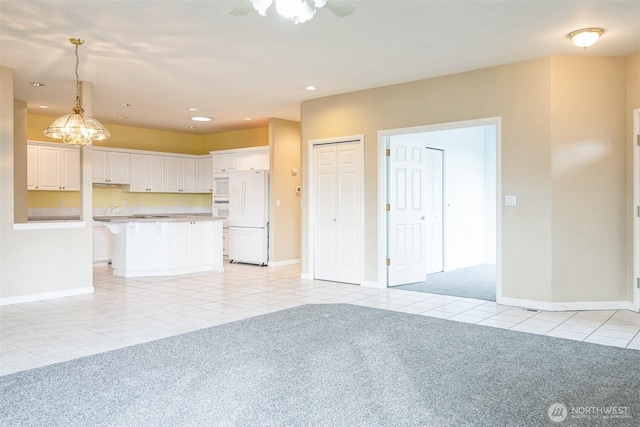 interior space featuring white appliances, white cabinetry, hanging light fixtures, a center island, and light carpet