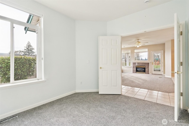 carpeted empty room with ceiling fan and a tile fireplace