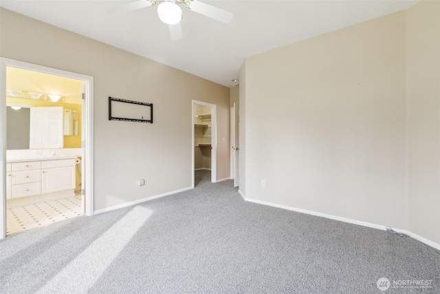 unfurnished bedroom with ensuite bathroom, a walk in closet, light colored carpet, ceiling fan, and a closet