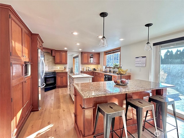 9305 SE Naples St, Moses Lake, WA 98837 - kitchen with light wood finished floors, tasteful backsplash, brown cabinetry, a center island, and black appliances