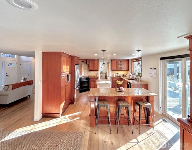 9305 SE Naples St, Moses Lake, WA 98837 - kitchen with a kitchen island, brown cabinets, black range with electric stovetop, freestanding refrigerator, and light wood-type flooring