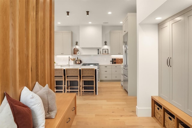 kitchen with white cabinetry, decorative backsplash, a kitchen bar, and light hardwood / wood-style floors