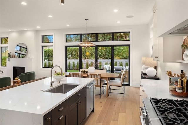 kitchen with sink, a kitchen island with sink, stainless steel appliances, light stone counters, and white cabinets