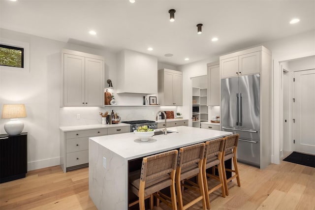 kitchen with built in fridge, an island with sink, sink, and light hardwood / wood-style flooring