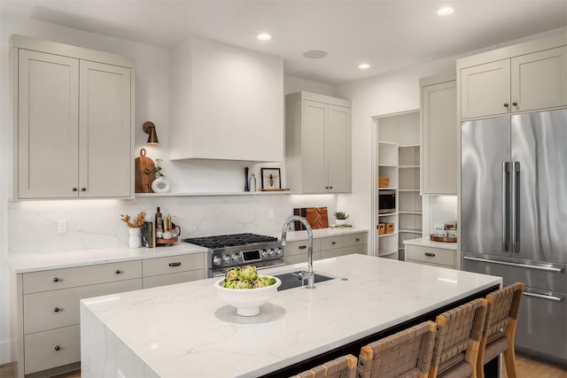 kitchen with high end appliances, light stone countertops, a kitchen island with sink, and tasteful backsplash