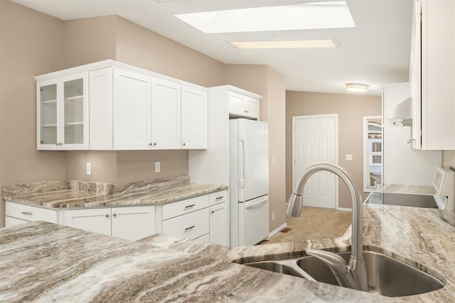 kitchen with white fridge, sink, white cabinets, and light stone counters