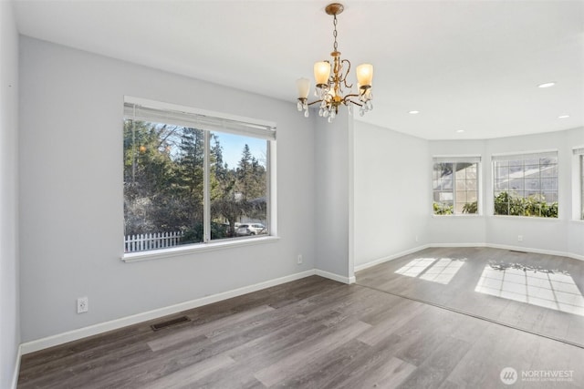 unfurnished dining area featuring visible vents, a notable chandelier, baseboards, and wood finished floors