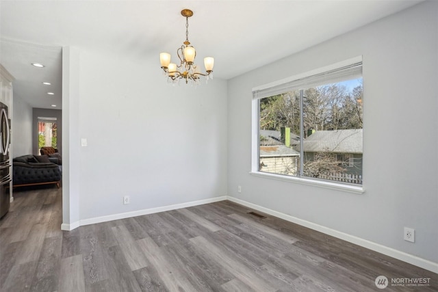 unfurnished room with a chandelier, visible vents, baseboards, and wood finished floors