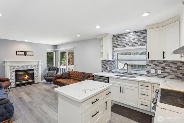 kitchen featuring open floor plan, a sink, a stone fireplace, backsplash, and range with electric stovetop