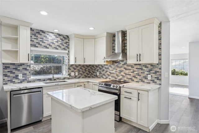 kitchen with appliances with stainless steel finishes, wood finished floors, wall chimney range hood, open shelves, and a sink