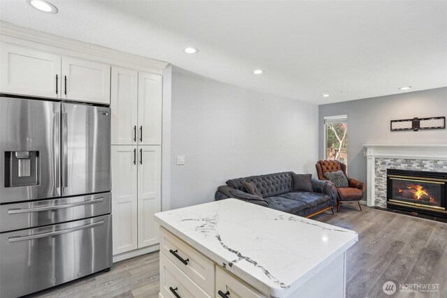 kitchen with light wood-style floors, stainless steel refrigerator with ice dispenser, a glass covered fireplace, and light stone countertops