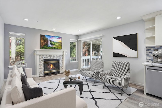 living area featuring baseboards, light wood-type flooring, a glass covered fireplace, and recessed lighting