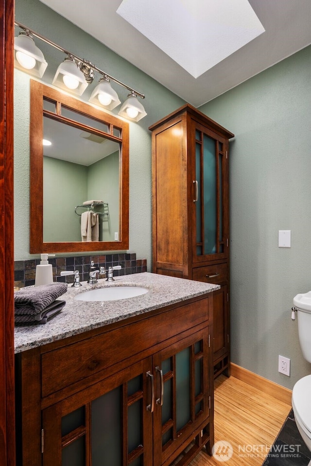 bathroom with baseboards, toilet, vanity, wood finished floors, and a skylight