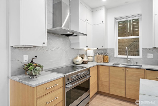 kitchen with light wood finished floors, wall chimney exhaust hood, high end stainless steel range, a sink, and backsplash