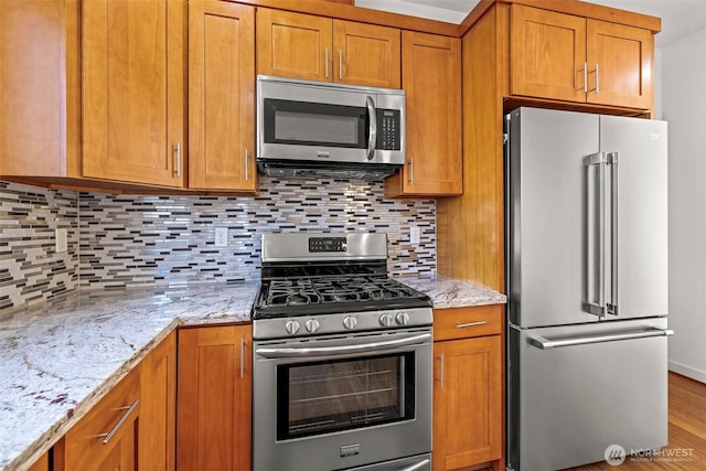 kitchen featuring backsplash, light stone countertops, light hardwood / wood-style floors, and appliances with stainless steel finishes