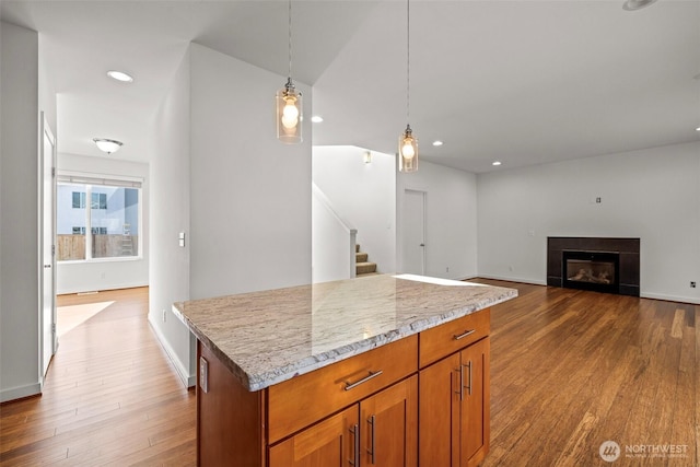 kitchen featuring hanging light fixtures, wood-type flooring, light stone countertops, and a center island