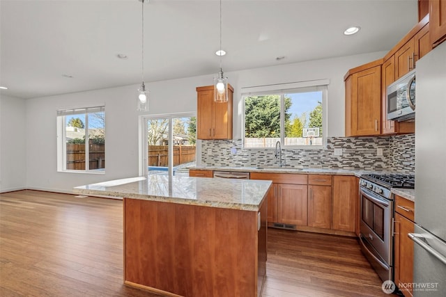 kitchen featuring sink, light stone counters, decorative light fixtures, a center island, and stainless steel appliances