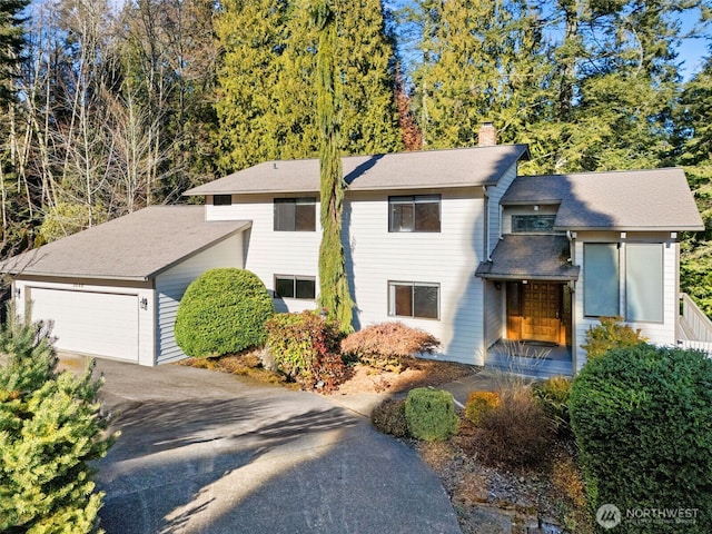 view of front of house with an attached garage, a chimney, and aphalt driveway