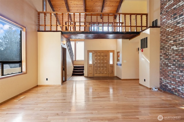 unfurnished living room with plenty of natural light, light wood-style flooring, a towering ceiling, and stairs