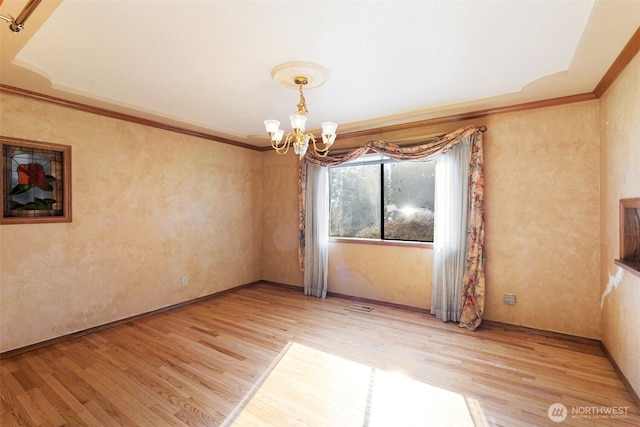 empty room with a chandelier, ornamental molding, and wood finished floors