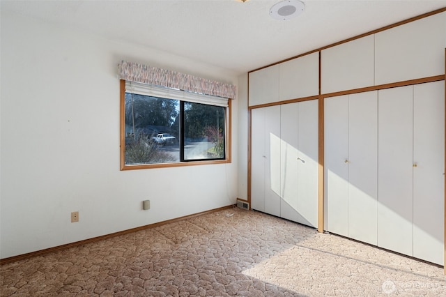 unfurnished bedroom featuring baseboards, visible vents, light colored carpet, and multiple closets