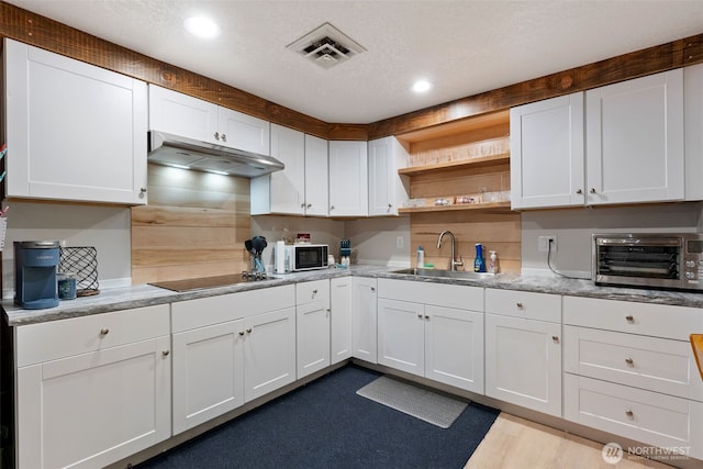 kitchen with black electric stovetop, visible vents, white cabinets, a sink, and under cabinet range hood