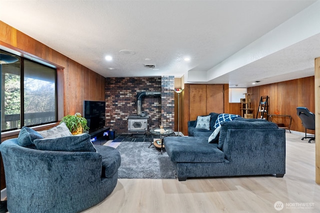 living room featuring visible vents, wood finished floors, a wood stove, a textured ceiling, and wood walls