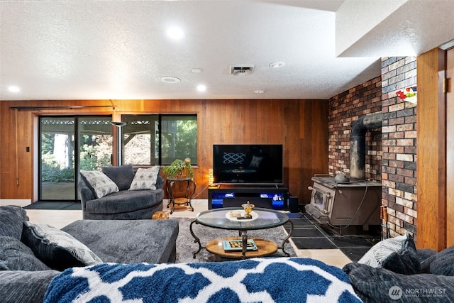 living room with a wood stove, wooden walls, visible vents, and a textured ceiling