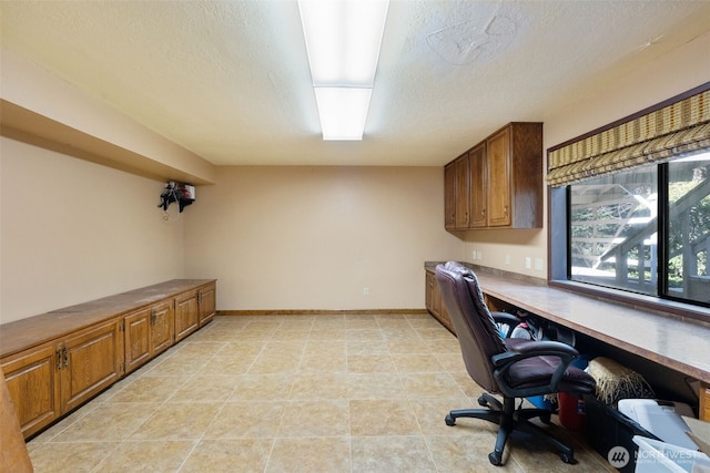 home office featuring a textured ceiling, built in desk, and baseboards