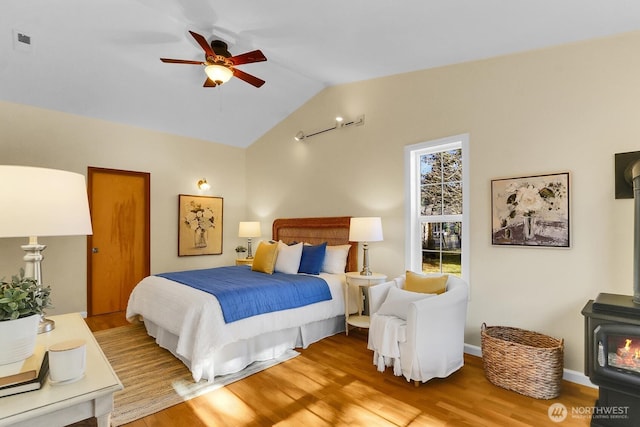 bedroom with ceiling fan, lofted ceiling, light hardwood / wood-style flooring, and a wood stove