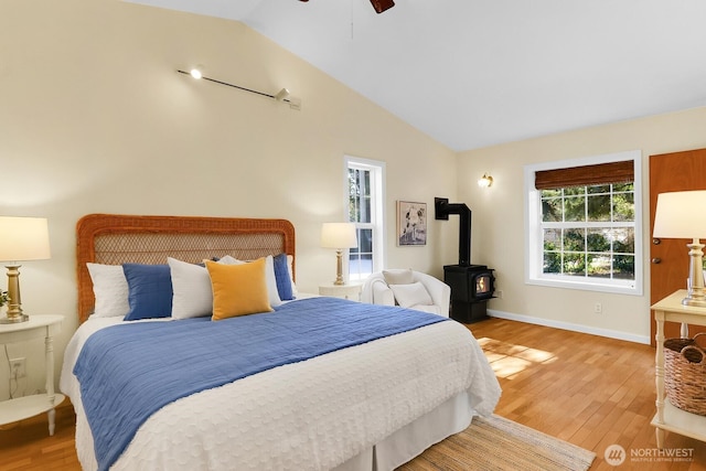 bedroom featuring ceiling fan, vaulted ceiling, light hardwood / wood-style flooring, and a wood stove