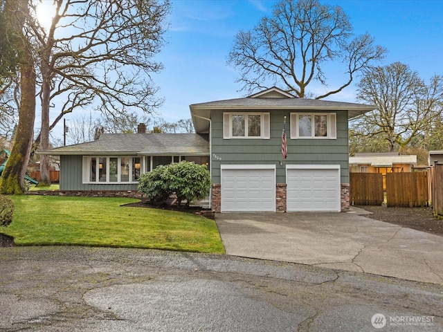 split level home featuring a front yard, fence, driveway, a garage, and brick siding