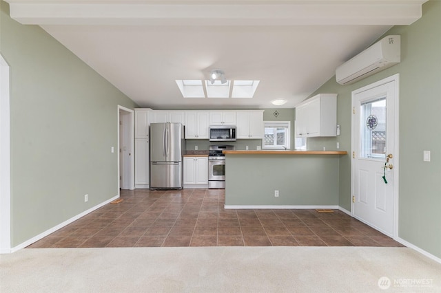 kitchen with baseboards, appliances with stainless steel finishes, a wall unit AC, and white cabinets